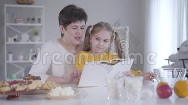 美丽的小女孩坐在祖母`膝盖上听食谱的肖像。 年轻的高加索祖母